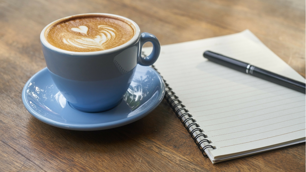 filled coffee cup and note book with pen on table